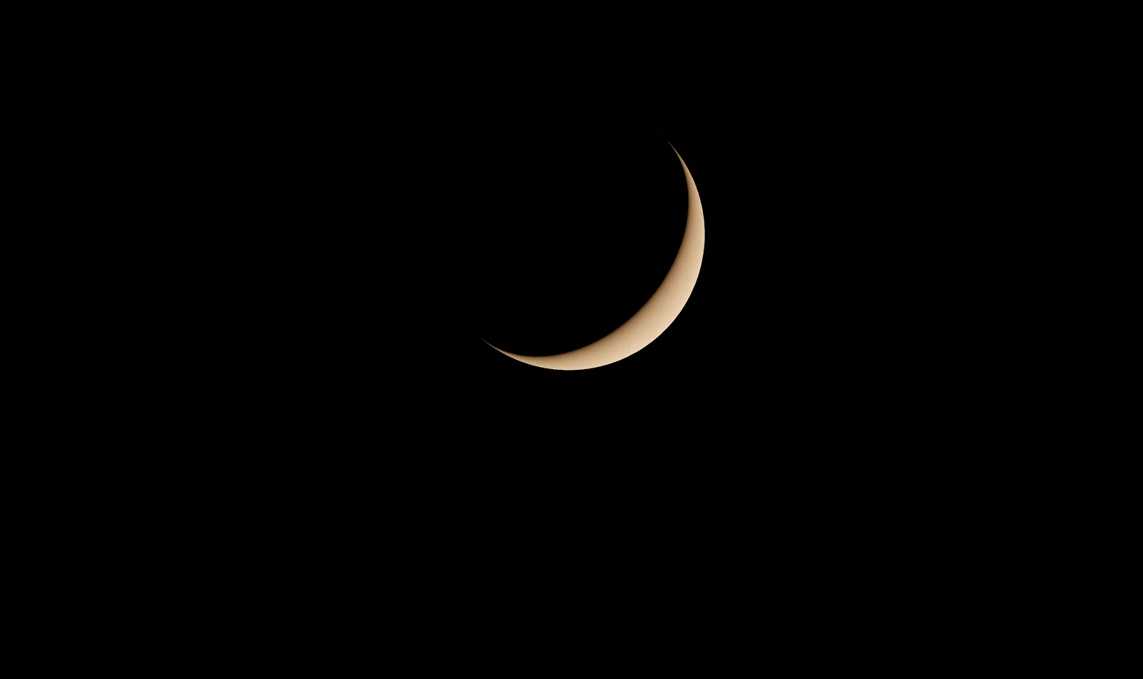 A thin, warm-tinted crescent moon against a black sky.