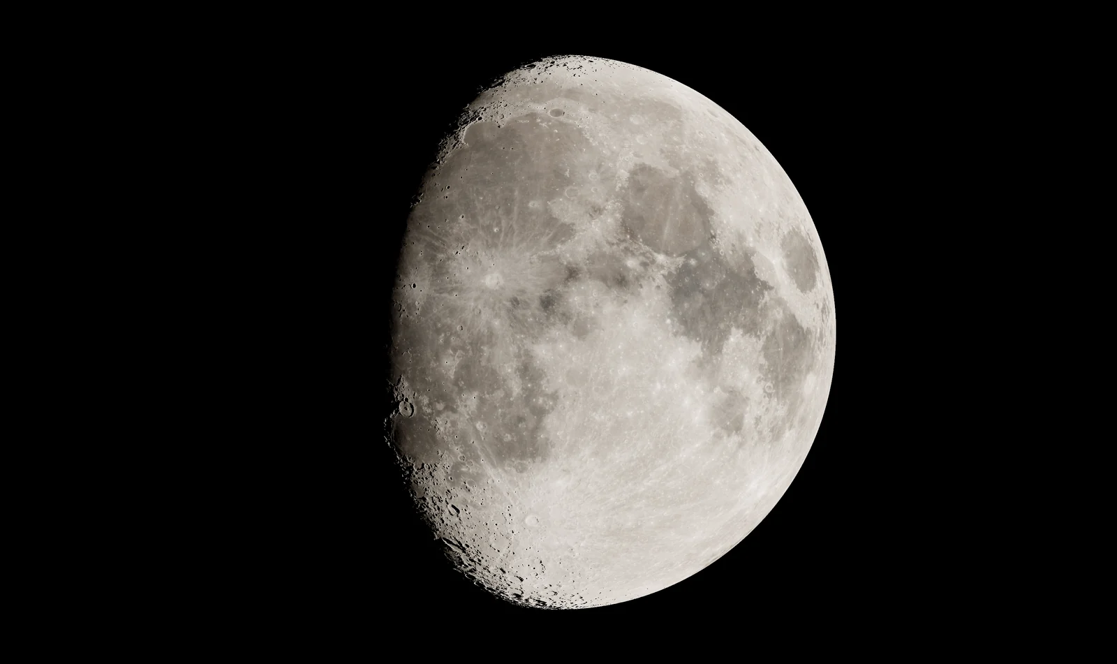 A waxing gibbous Moon filling the view, its gray seas and bright craters sharp, with a crater-lined edge where its day meets its night.