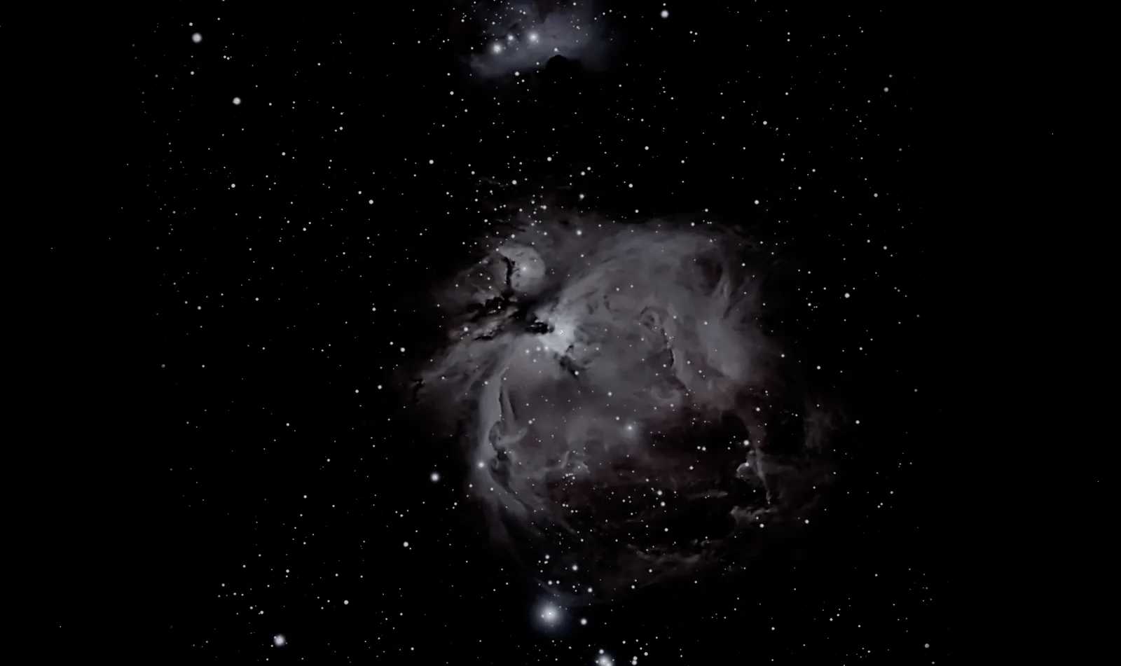 The Orion Nebula, a gray cloud with a bright heart and sweeping wings, among the stars, with a smaller cloud above it.